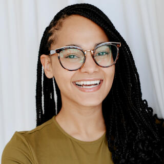 a headshot of a girl with a gold top on and long black hair with glasses