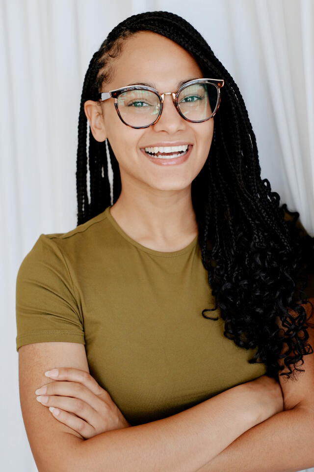 a headshot of a girl with a gold top on and long black hair with glasses