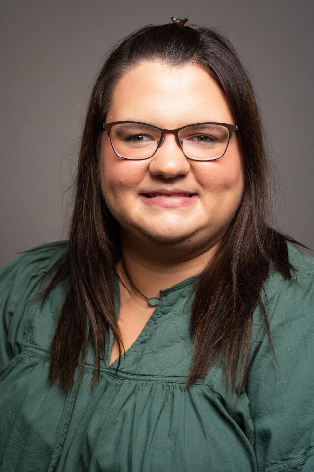 a headshot of a woman wearing a green top with long dark hair and glasses