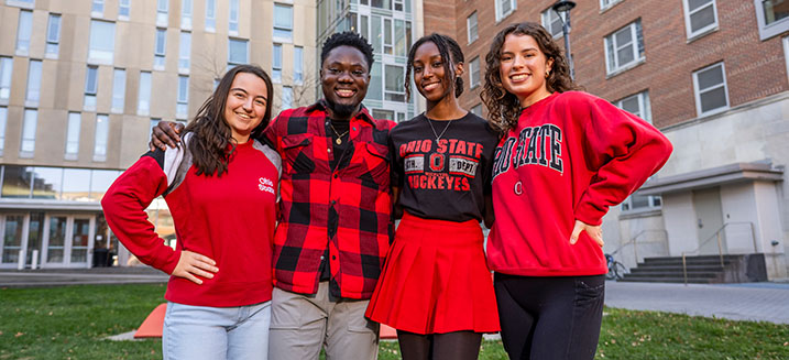 Four students wearing scarlet posing in front of residence halls.